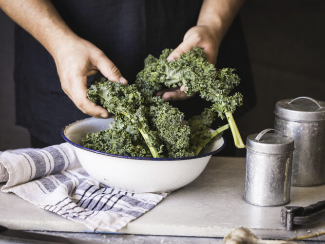 person holding kale over a bowl