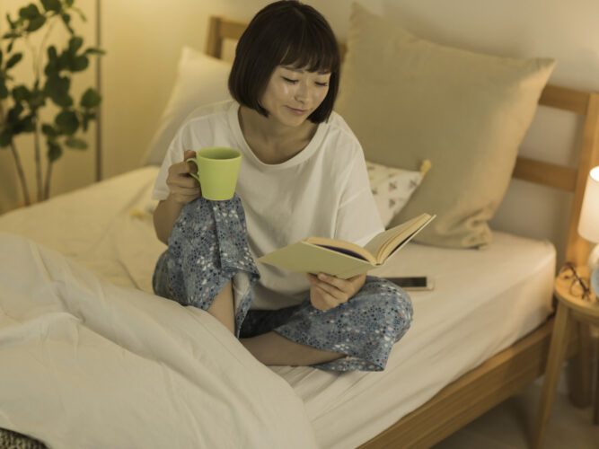 woman sipping on tea reading a book in bed