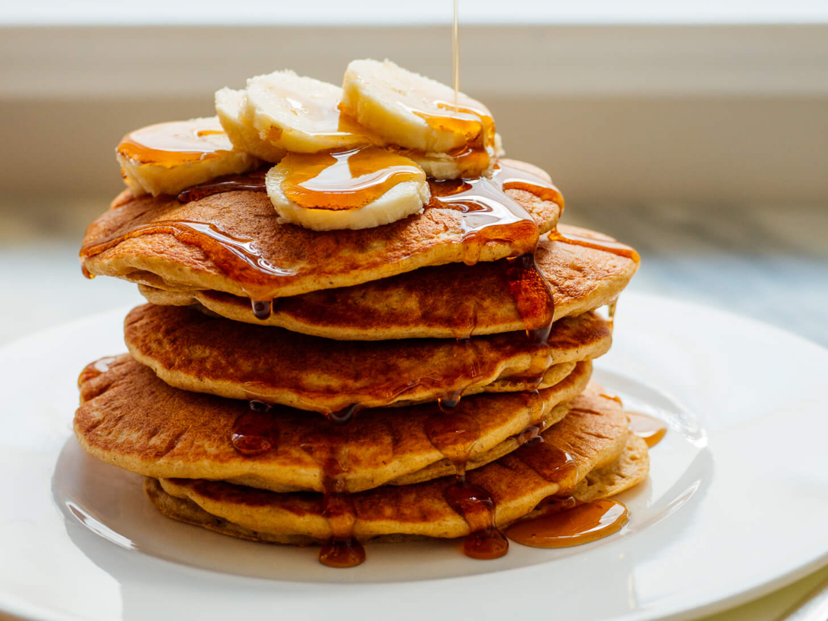 blender oatmeal pancakes stacked on a plate with bananas and syrup