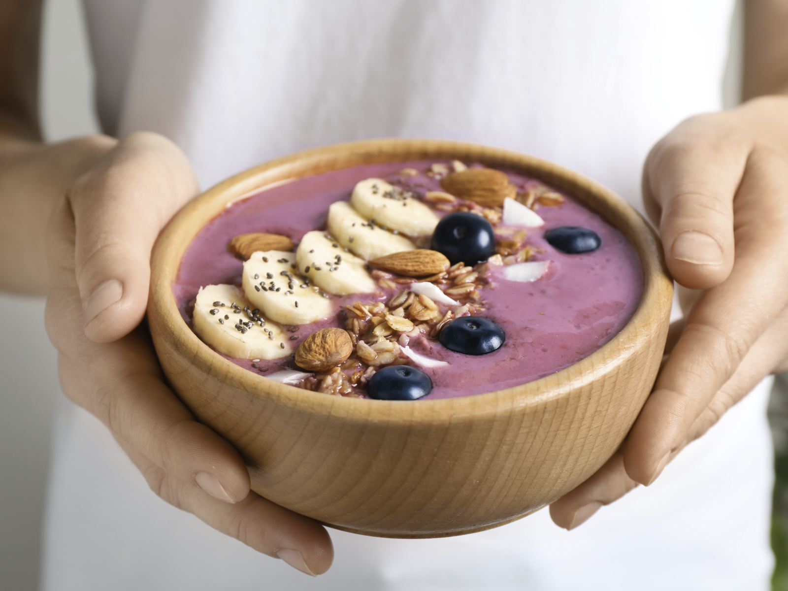 woman holding breakfast smoothie bowl with fruit and almonds