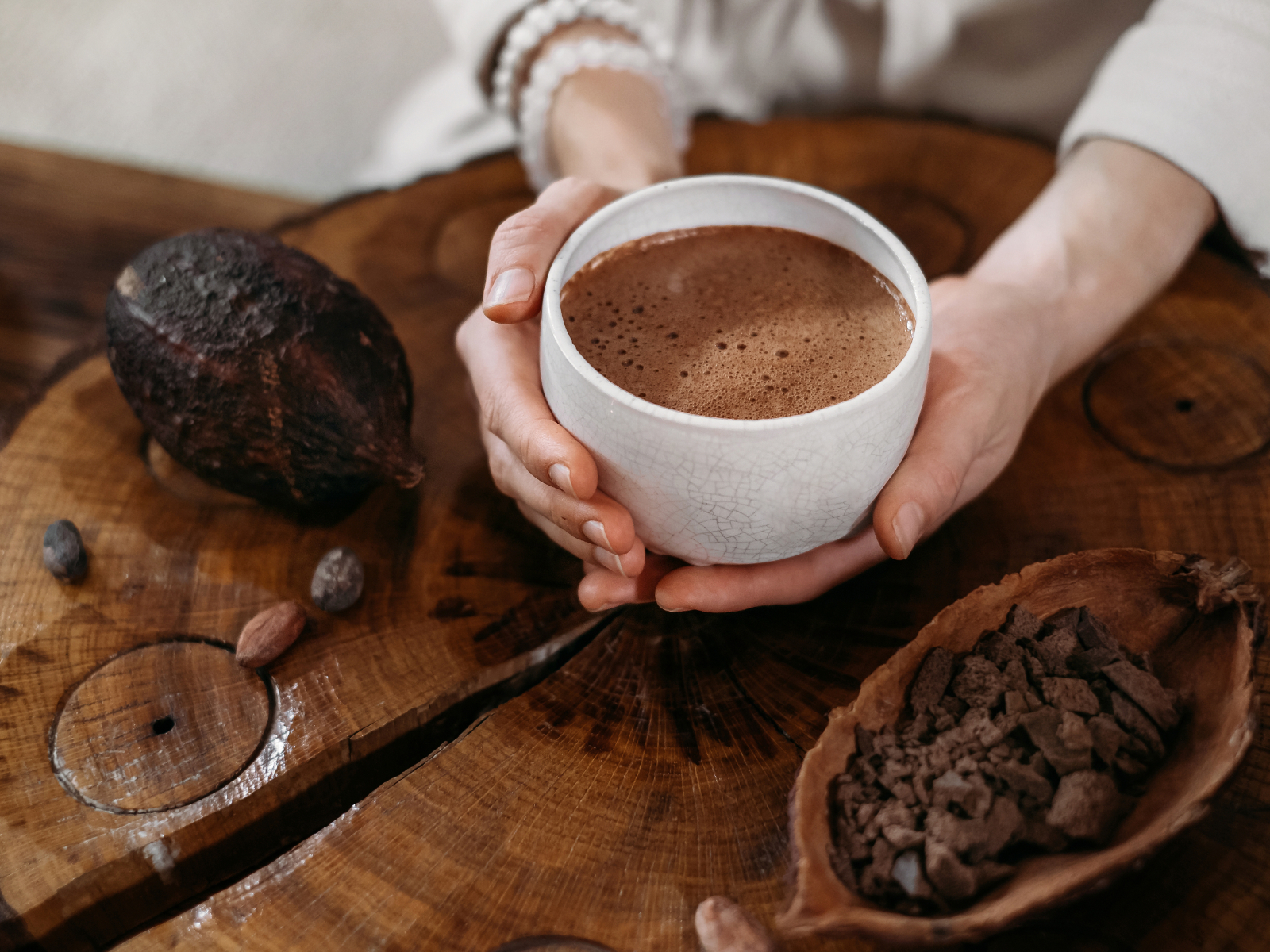 person holding cup of hot chocolate next to a whole cacao bean