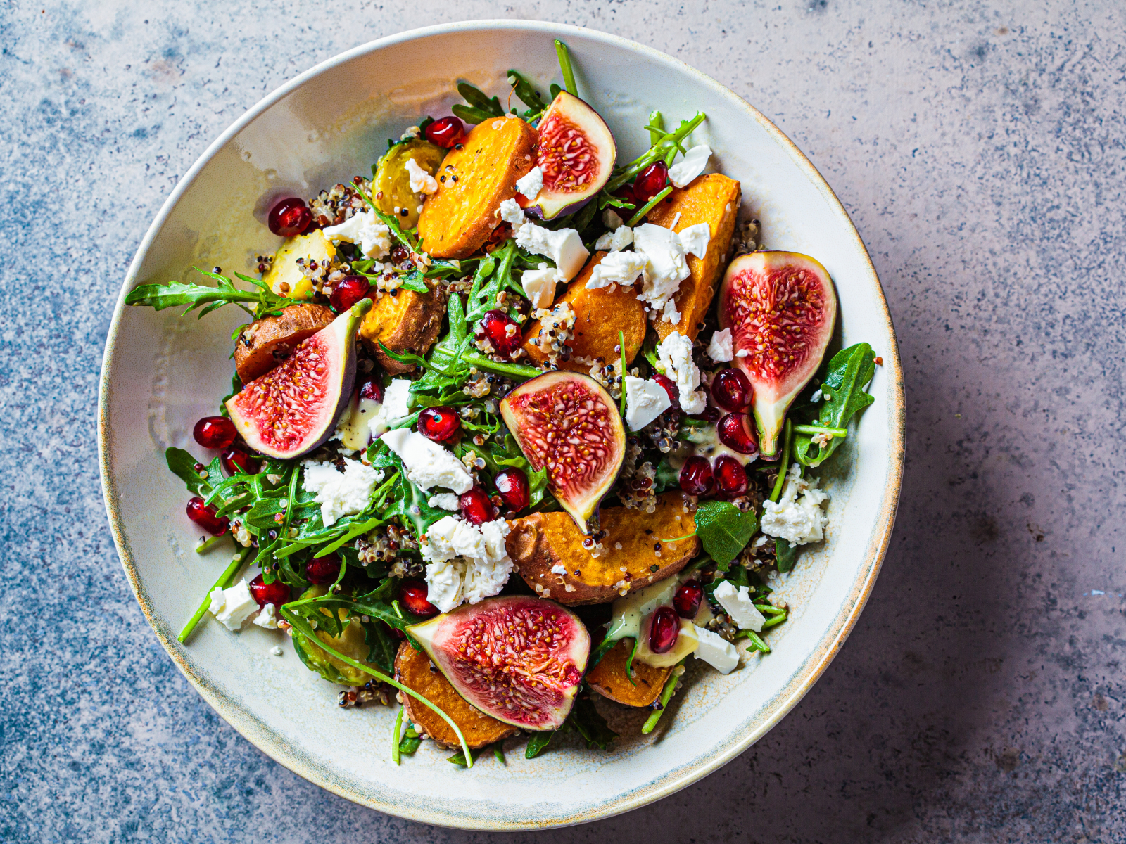 a hearty christmas salad with roasted veggies, figs, feta cheese, and pomegranate seeds