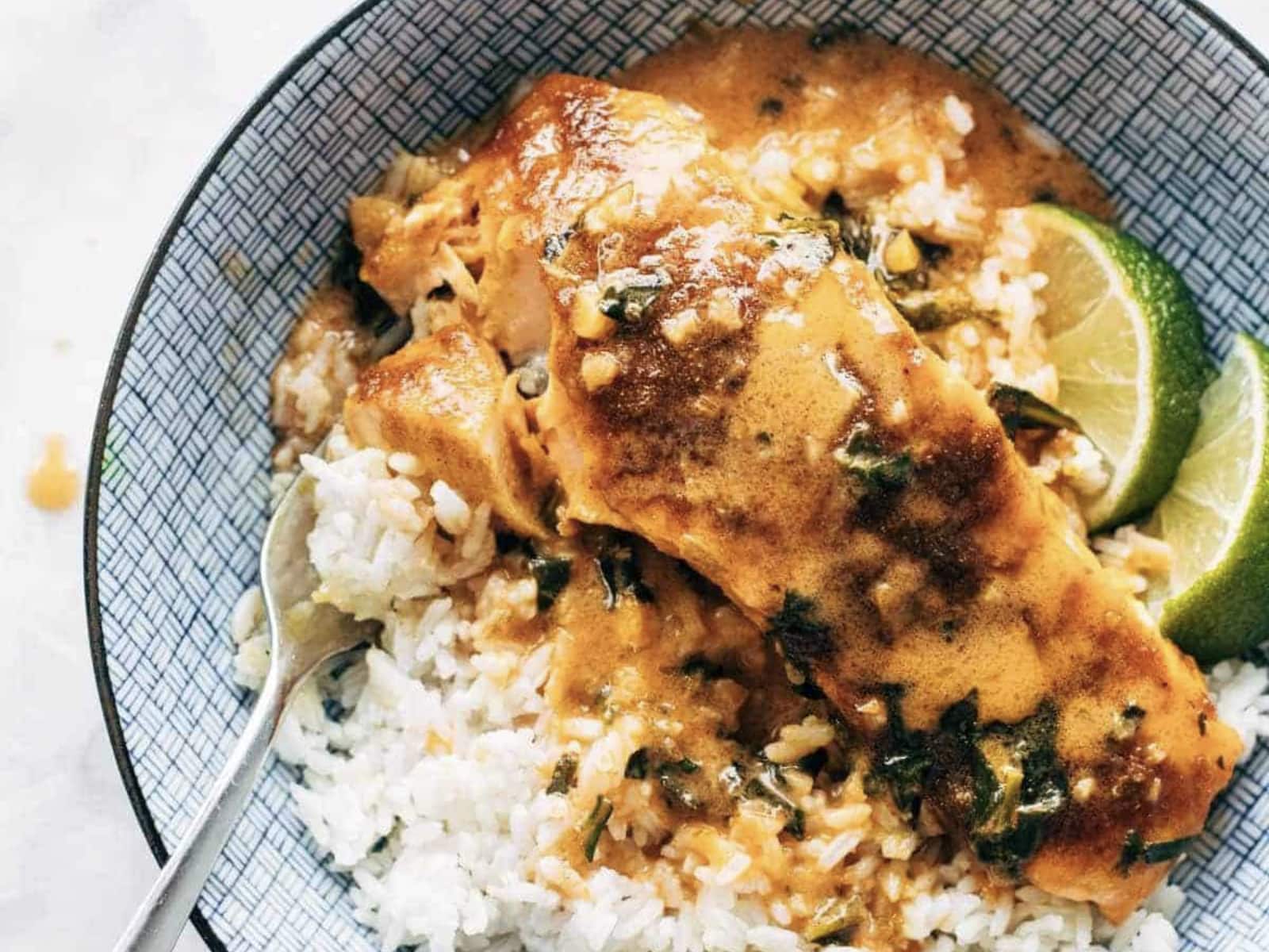coconut curry salmon in a bowl with rice and limes