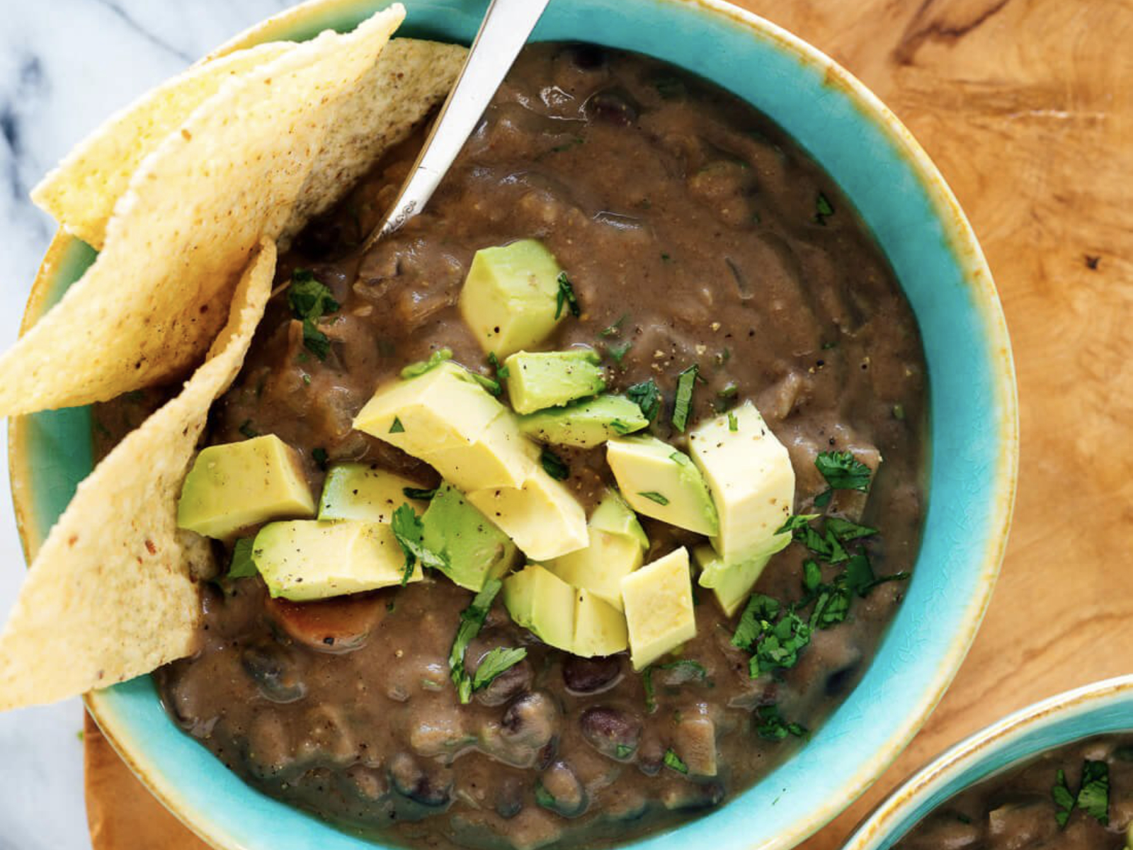 crock pot black bean soup in a bowl with tortilla chips and diced avocado