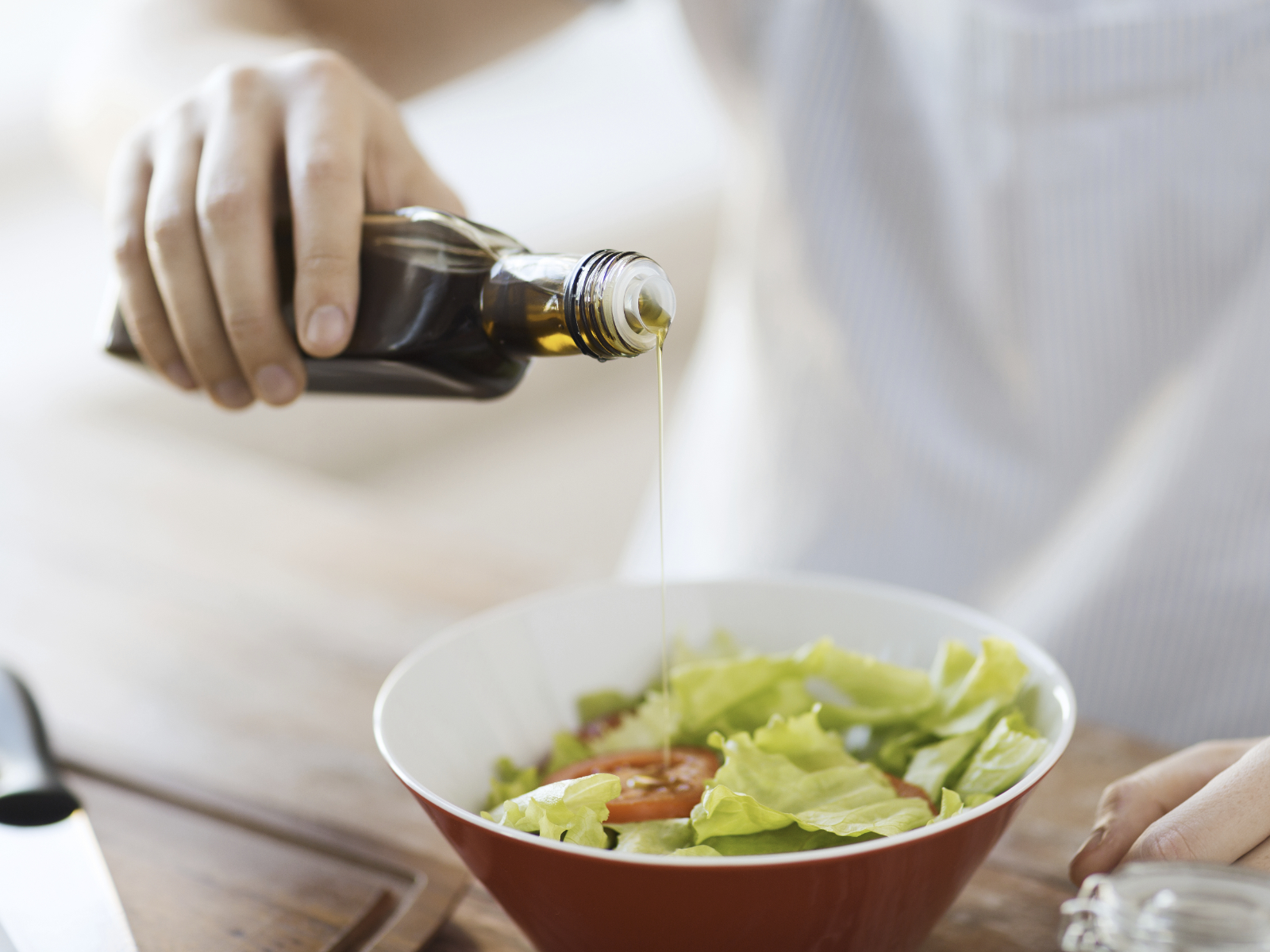 man drizzling olive oil onto a salad