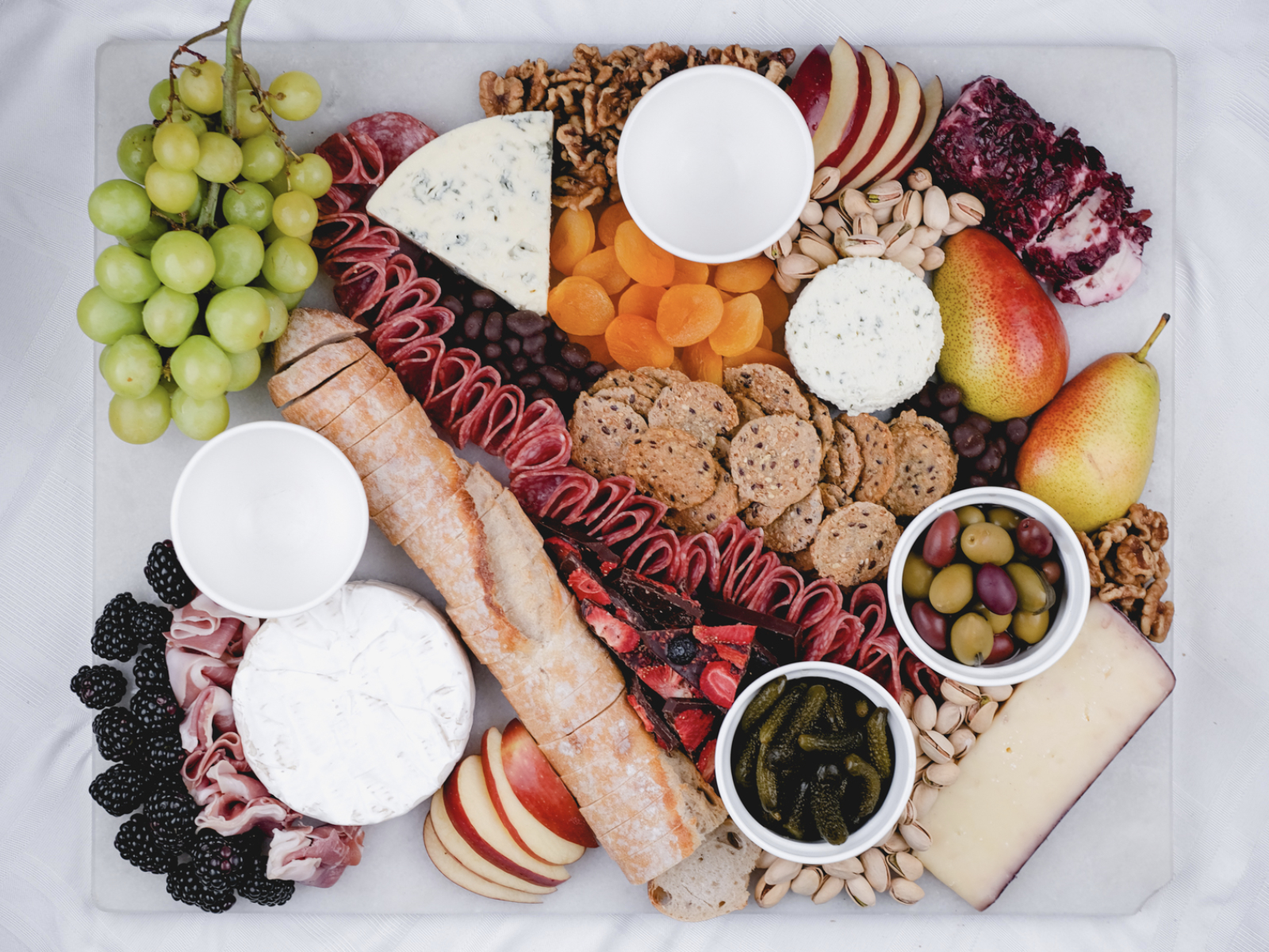 adding bread, crackers, nuts, and chocolate to a grazing board