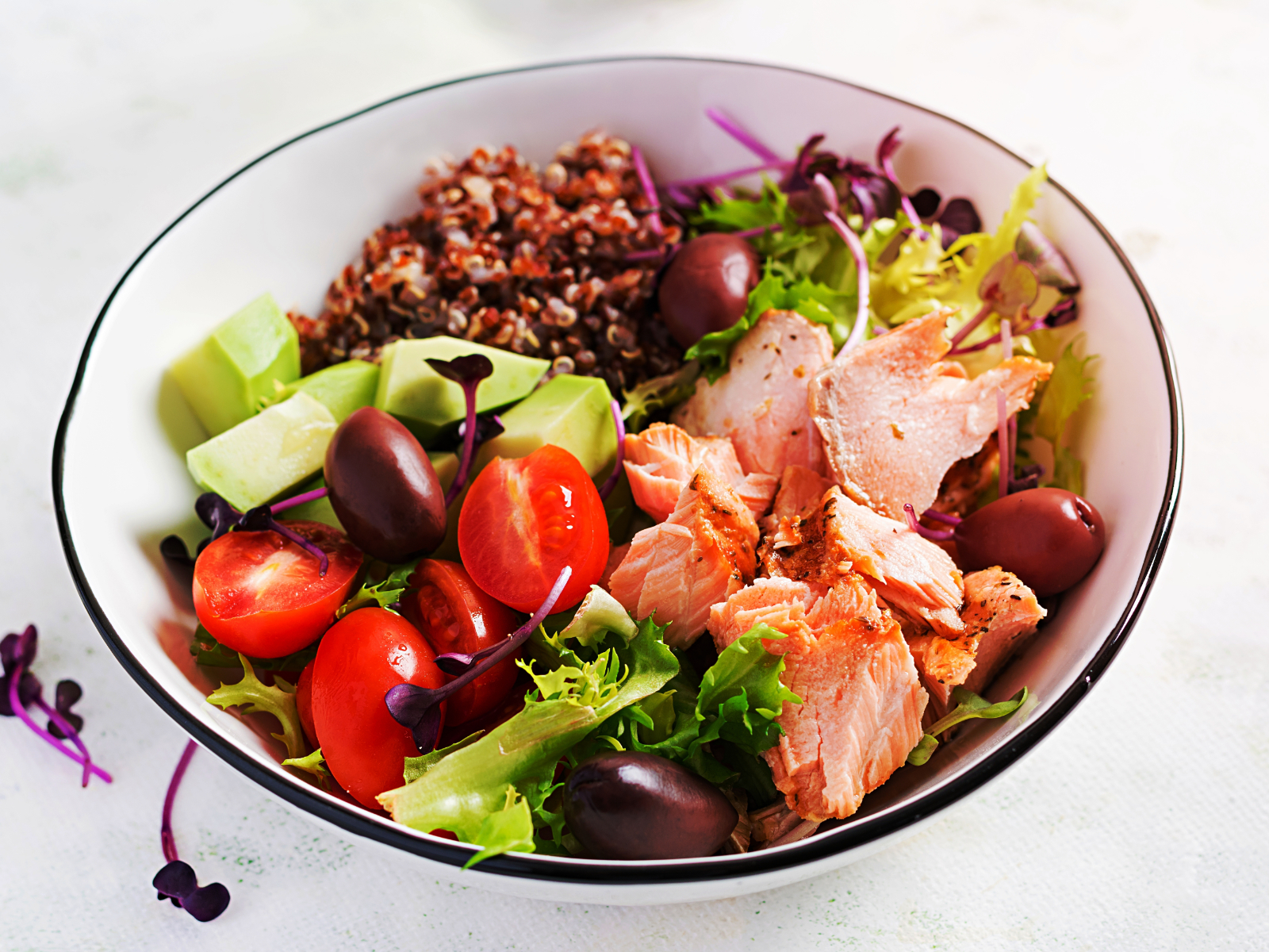 A mixed green salad with grilled salmon, avocado, and cherry tomatoes