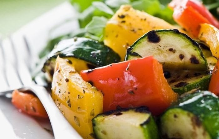 Plate of grilled vegetables with arugula salad on a green background