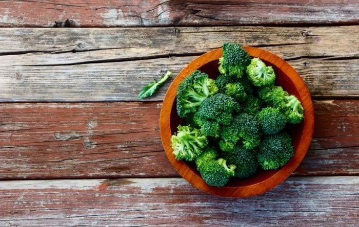 Fresh green broccoli in wood bowl over rustic wooden background - healthy or vegetarian food concept Top view.