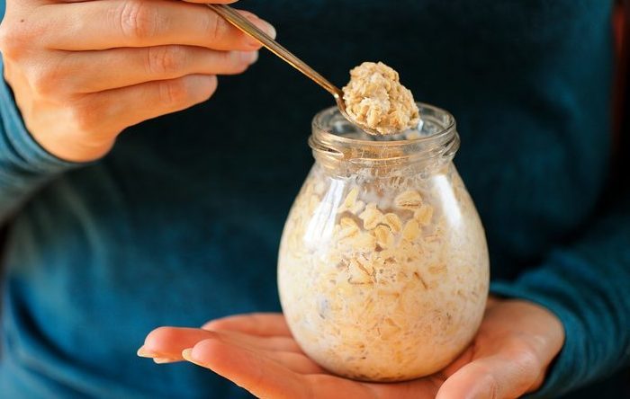 Woman's slender hands holding glass jar and spoon with overnight oats closeup selective focus horizontal
