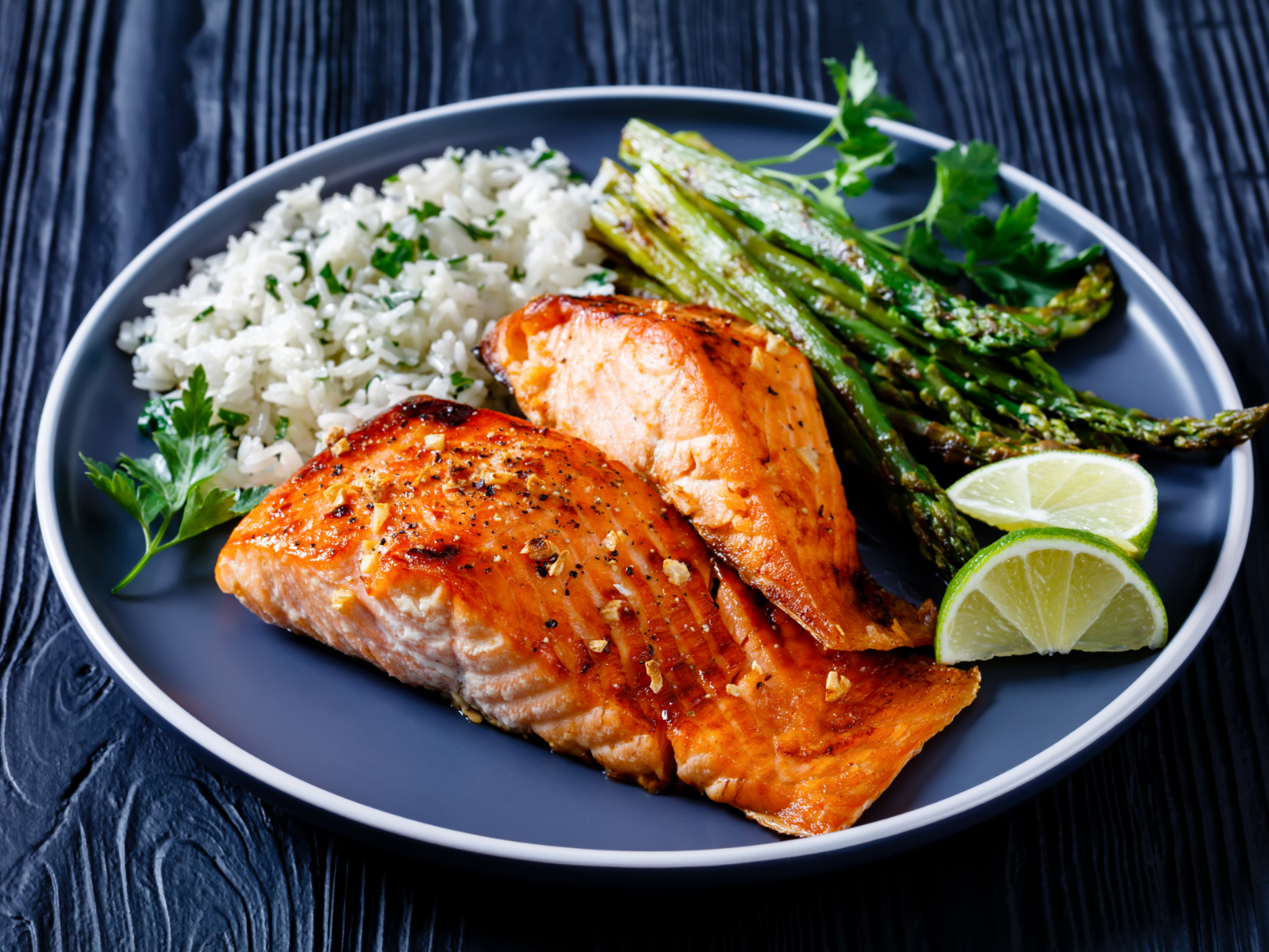 salmon fillets on a plate with rice asparagus and lime wedges