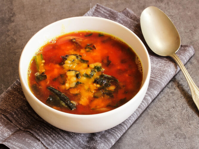 lentil soup with tomatoes and spinach in a bowl with a gold spoon