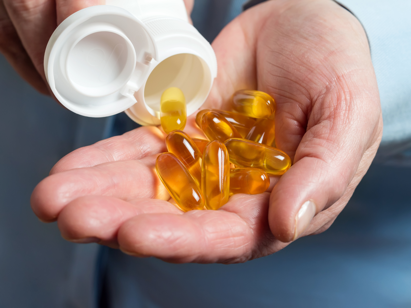 person holding a handful of omega 3 fatty acid supplements from a pill bottle