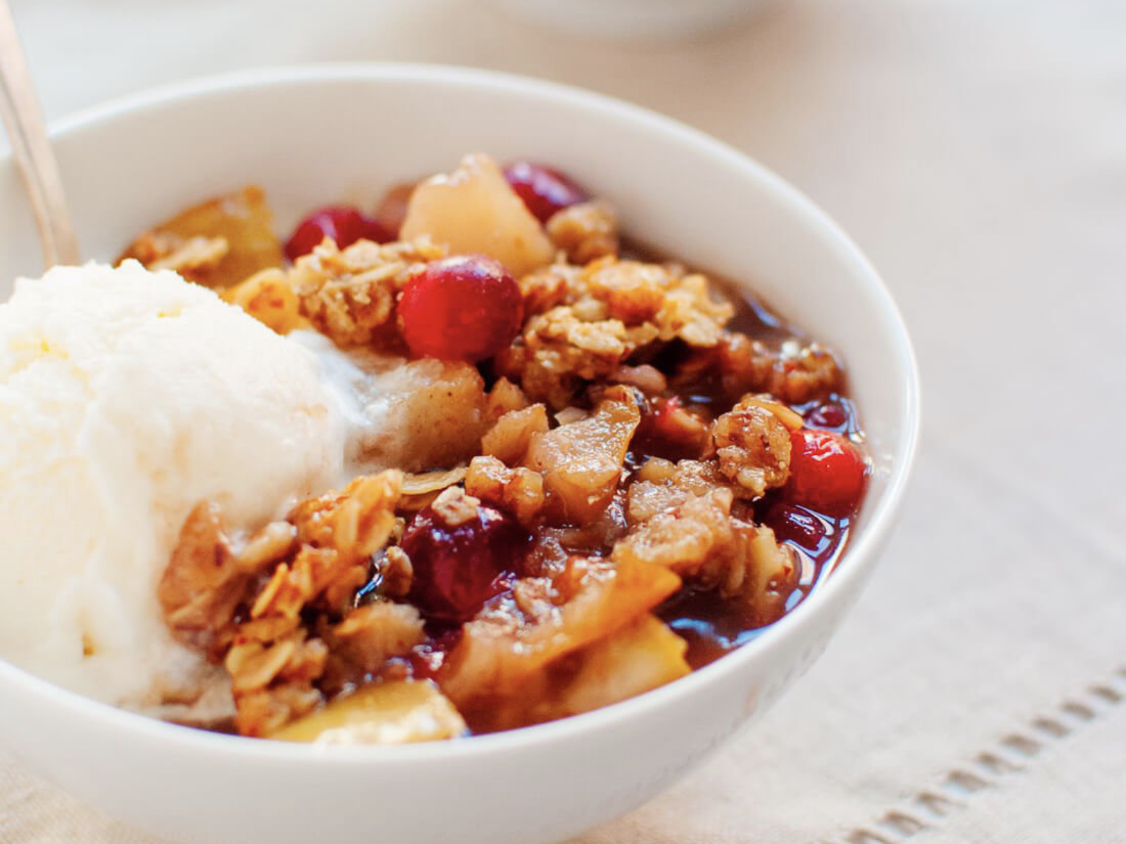 bowl of pear cranberry crisp with a scoop of vanilla ice cream
