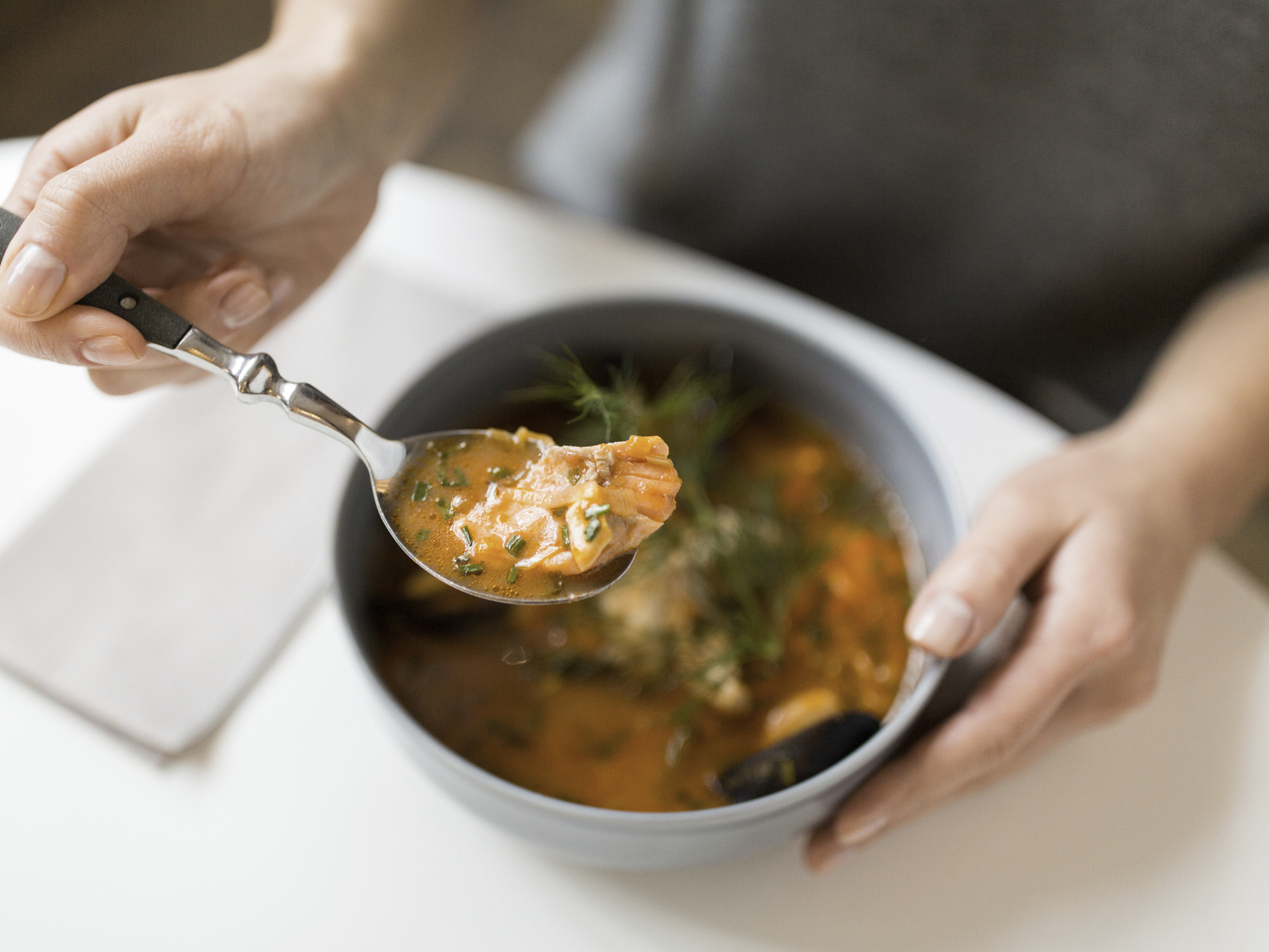 person with spoonful of soup with seafood in it