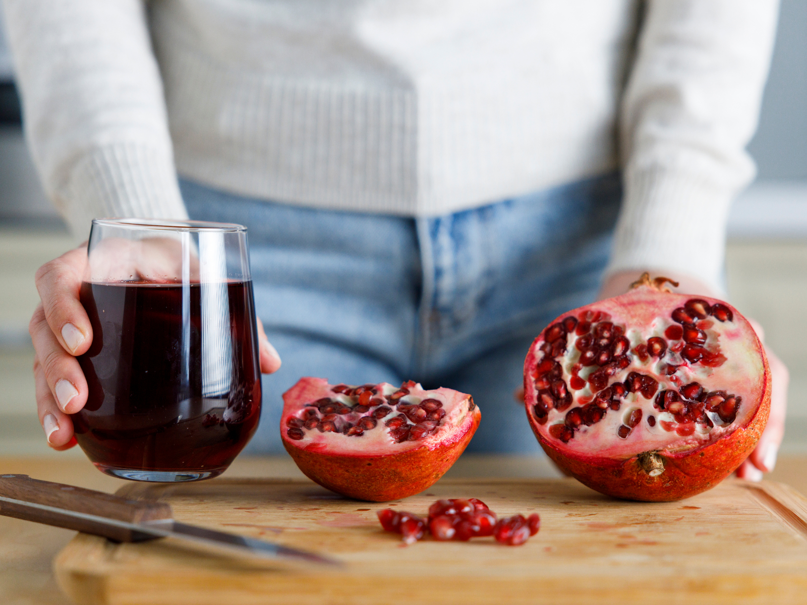 person with pomegranate juice next to a cut pomegranate fruit