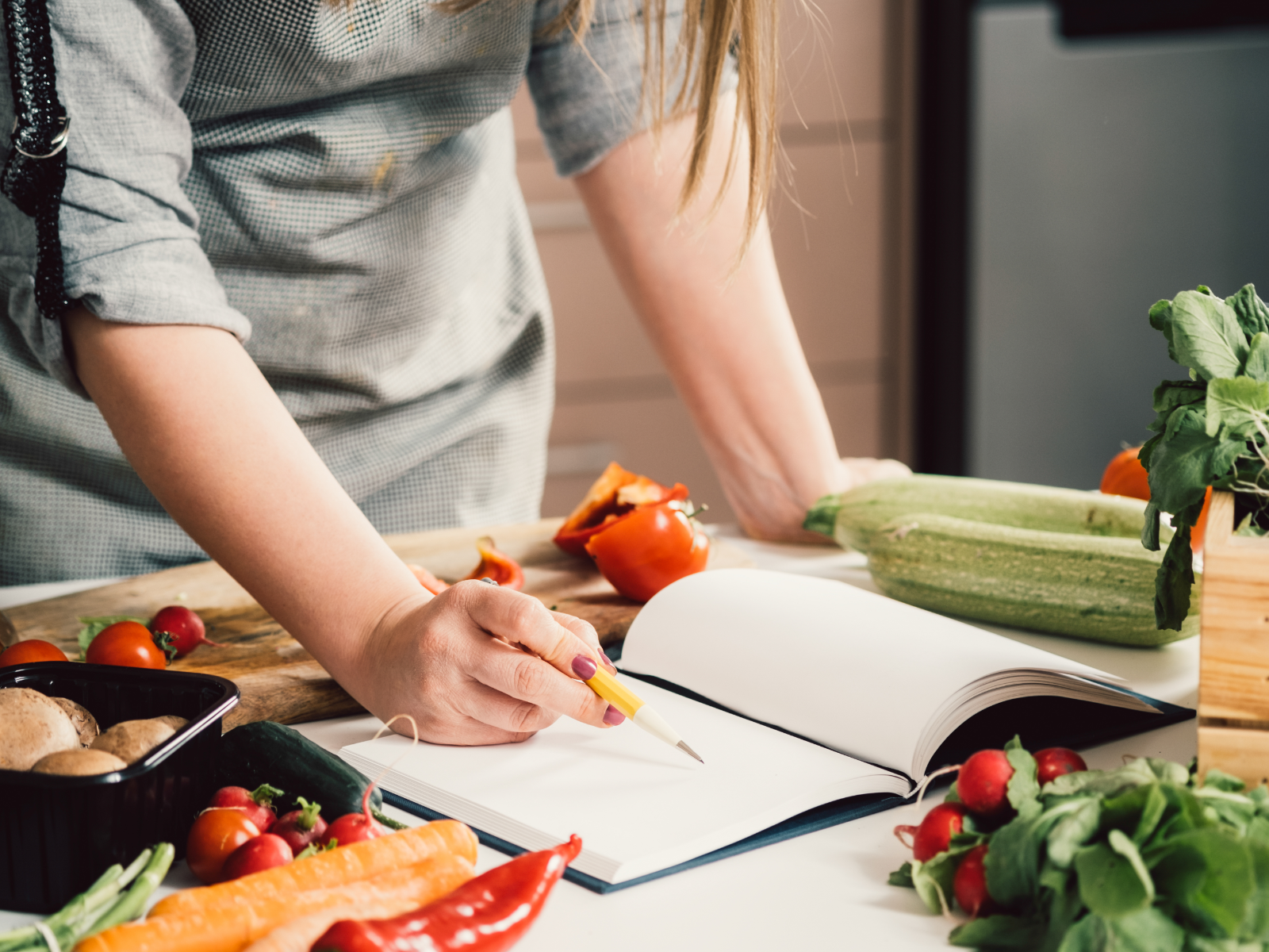 woman marking a cookbook surrounded by healthy vegetables