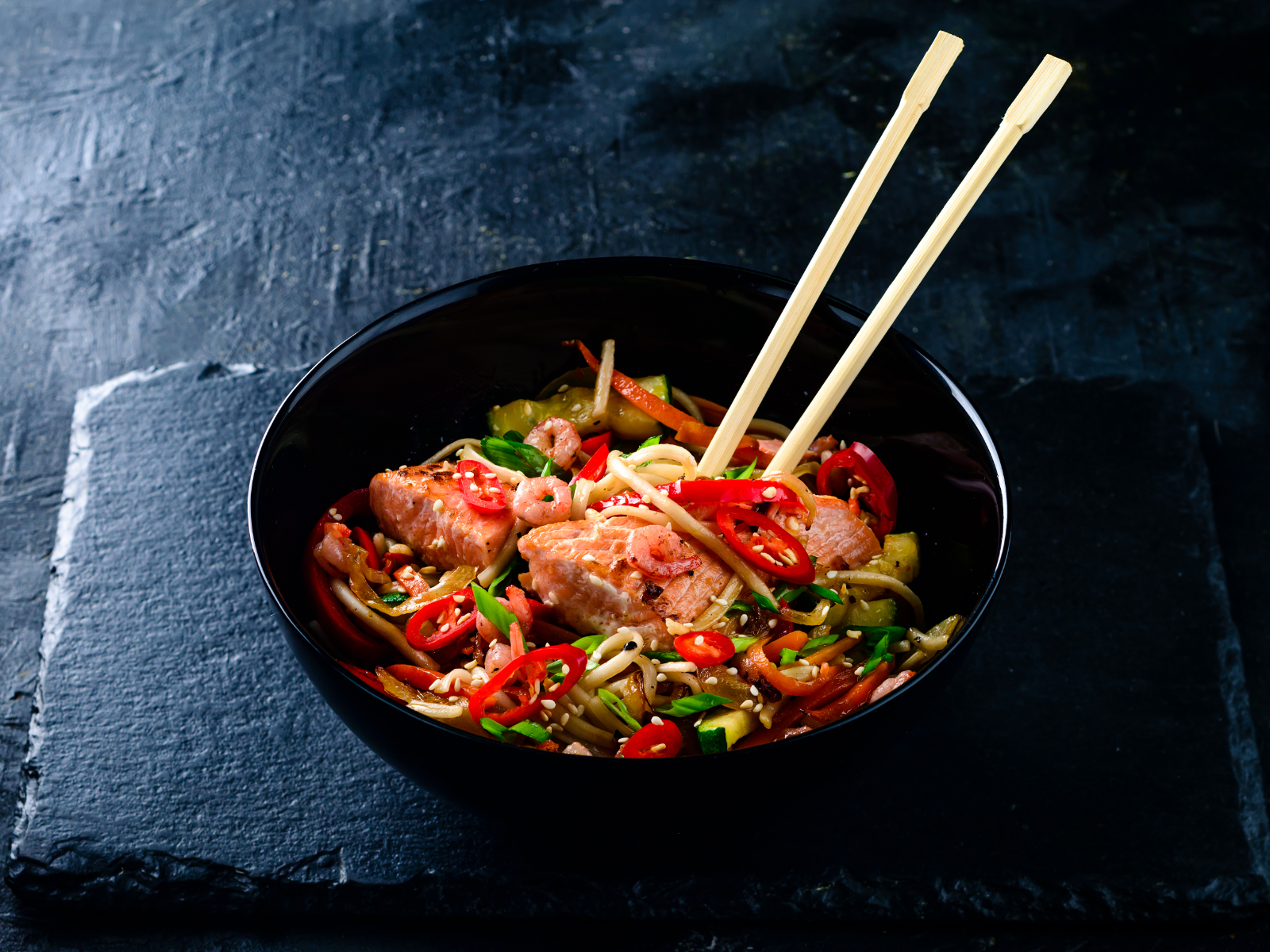 salmon and vegetable noodle stir fry in a bowl with chopsticks