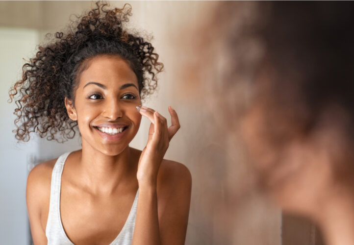 Beautiful Black woman smiling in the mirror as she does her skincare routine