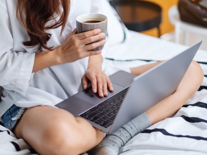 an image of a woman working from bed with her laptop and a cup of coffee