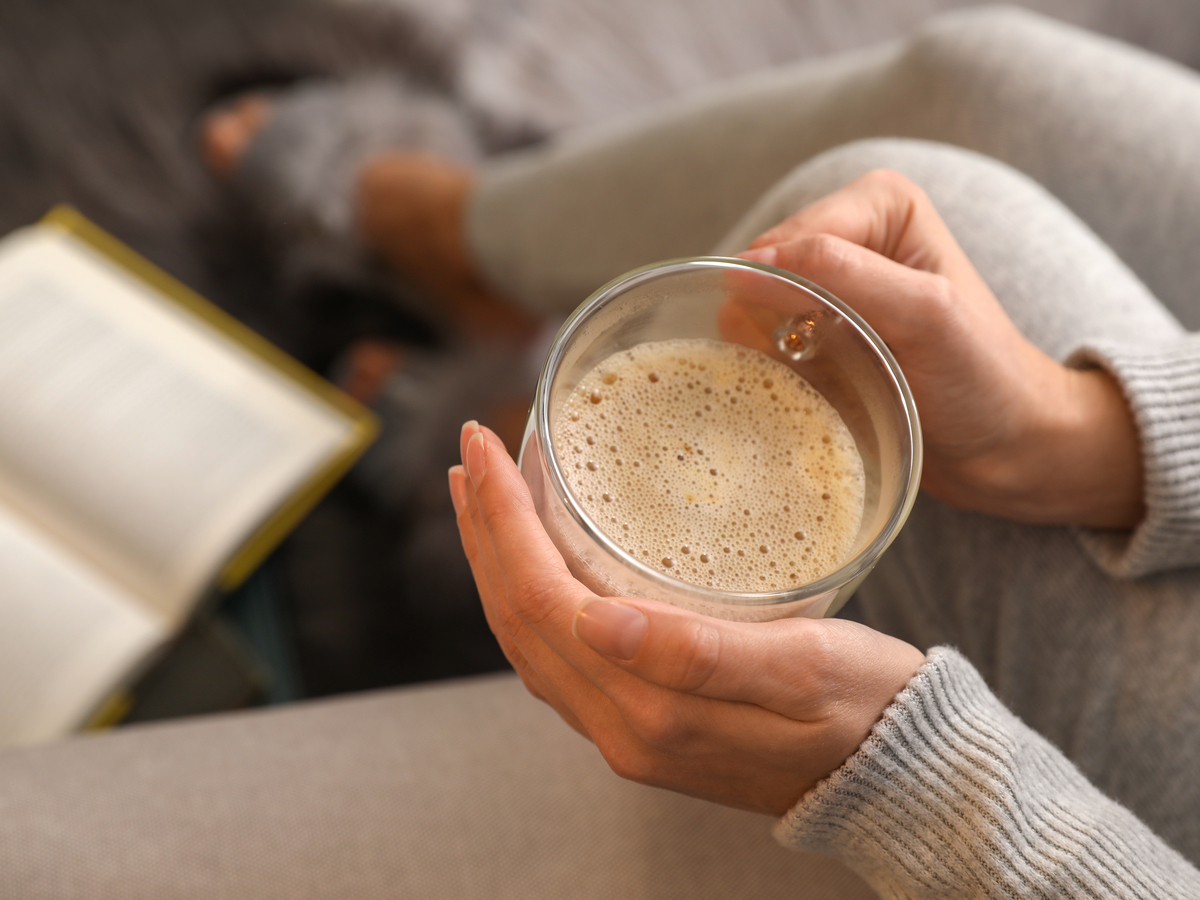 woman holding coffee with cream on couch reading a book