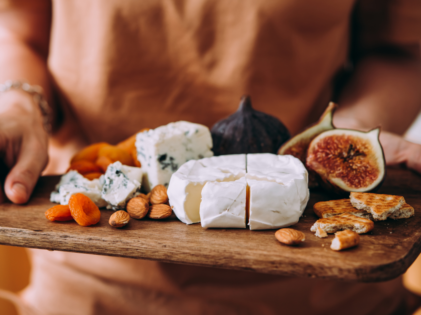 woman holding a small cheese plate with whole grain crackers, nuts, and fruit