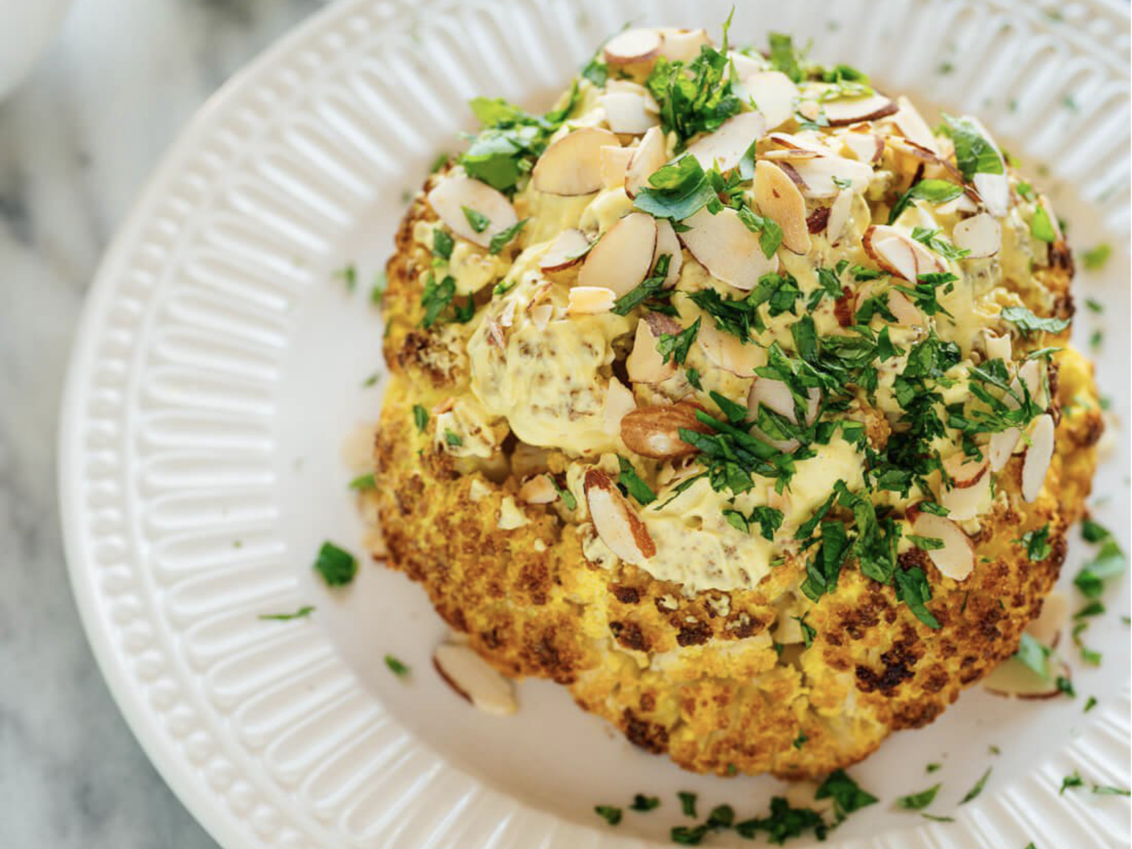 whole roasted cauliflower with nuts and herbs on top