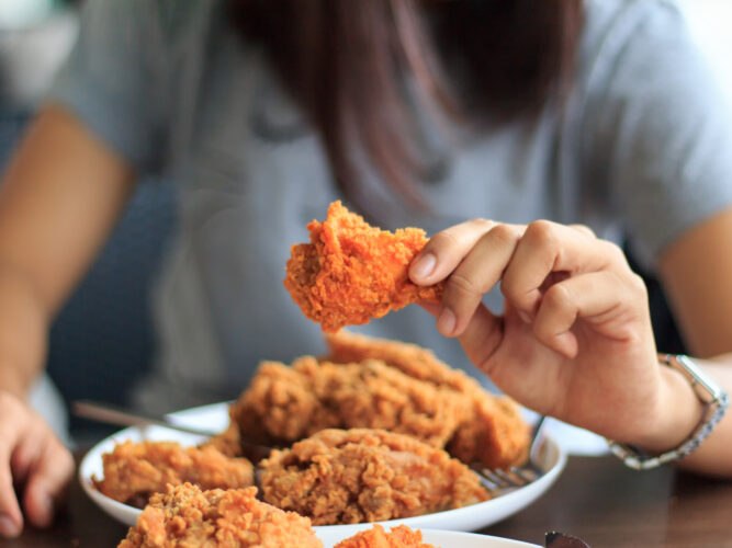 woman picking up a piece of fried chicken from a plate