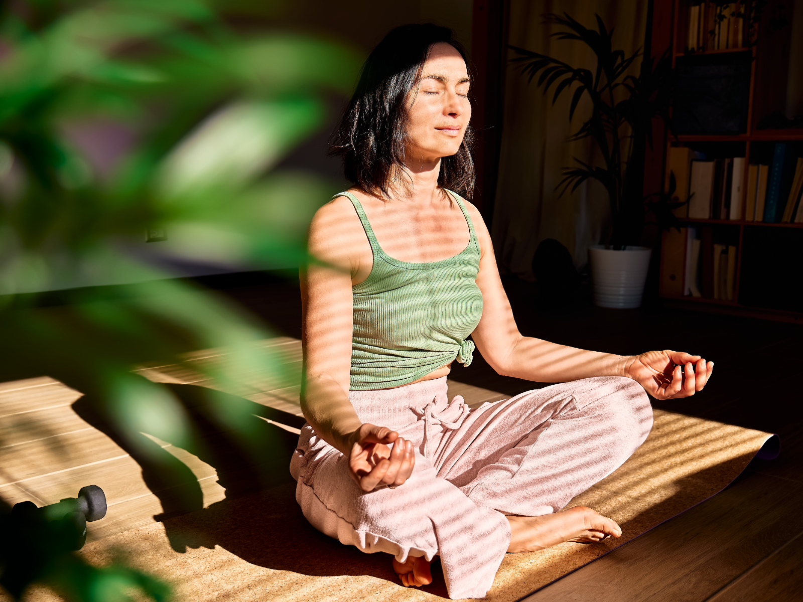 woman meditating next to a sunny window and plant