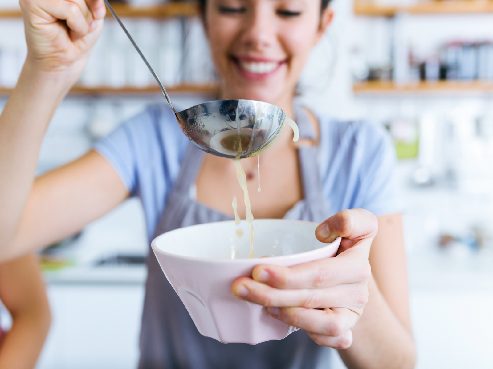 woman serving herself broth with a ladle into a bowl